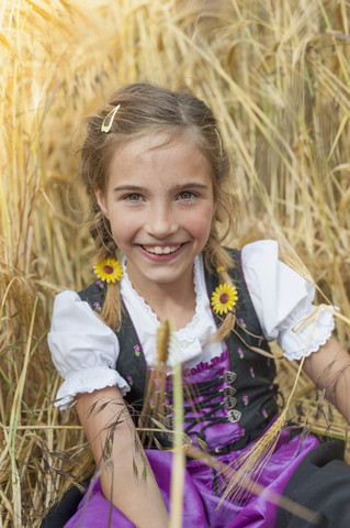 Deutschland, Sachsen, Porträt eines lächelnden Mädchens im Dirndl, das auf einem Feld sitzt, lizenzfreies Stockfoto