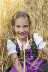 Deutschland, Sachsen, Porträt eines lächelnden Mädchens im Dirndl, das auf einem Feld sitzt - MJF001583