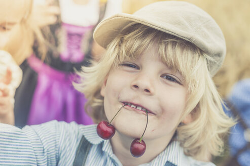 Porträt eines kleinen Jungen, der zwei Kirschen im Mund hält - MJF001587