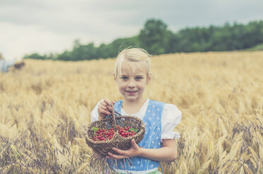 Germany, Saxony, portrait of smiling girl standing in a grain field with basket of red currants - MJF001589