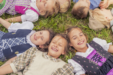 Deutschland, Sachsen, Gruppe von Kindern in traditioneller Kleidung auf einer Wiese im Kreis liegend - MJF001596