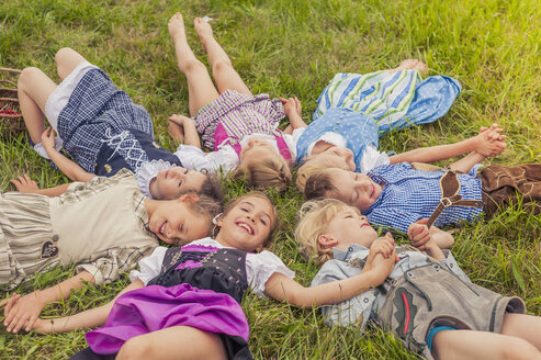 Deutschland, Sachsen, Gruppe von Kindern in traditioneller Kleidung auf einer Wiese im Kreis liegend - MJF001597
