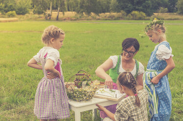 Germany, Saxony, three little girls and their educator in traditonal clothes on a meadow - MJF001615