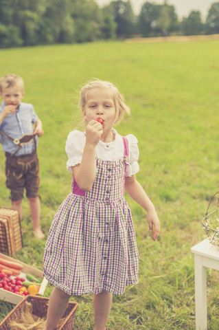 Deutschland, Sachsen, Porträt eines Mädchens im Dirndl, das einen roten Rettich isst, lizenzfreies Stockfoto