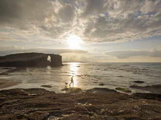 Spain, Galicia, Ribadeo, Playa de Aguas Santas at sunset, person and dog on the beach - LAF001410