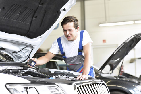 Mechaniker untersucht den Motor eines Autos in einer Werkstatt - LYF000429