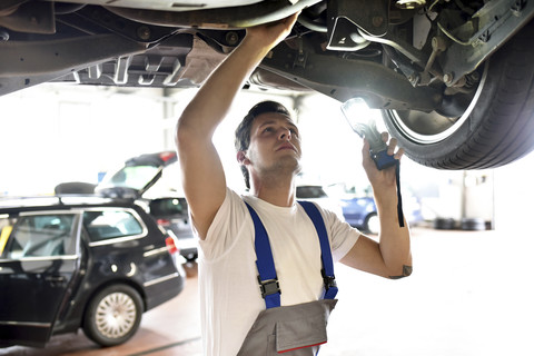 Mechaniker untersucht den Unterboden eines Autos in einer Werkstatt, lizenzfreies Stockfoto