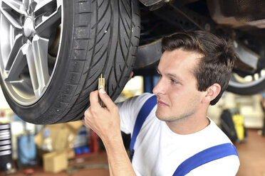 Mechaniker misst das Reifenprofil eines Autos in einer Werkstatt - LYF000449