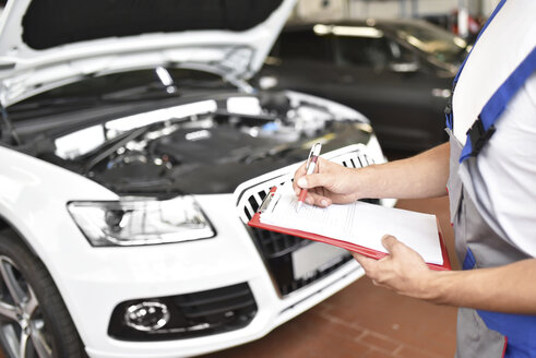 Car mechanic holding clipboard in a garage - LYF000435