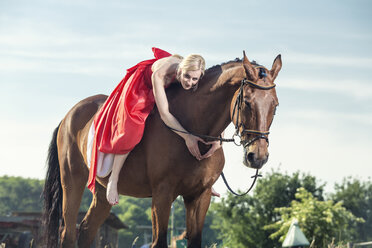 Porträt einer jungen Frau in rotem Abendkleid, die auf einem Pferd sitzt und mit ihren Händen eine Herzform bildet - TAMF000244