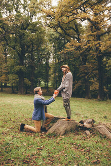 Junger Mann kniet nieder und macht seiner Freundin in einem herbstlichen Park einen Heiratsantrag - CHAF000201