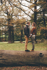 Junges verliebtes Paar, das sich auf einem Baumstamm in einem herbstlichen Park an den Händen hält - CHAF000203