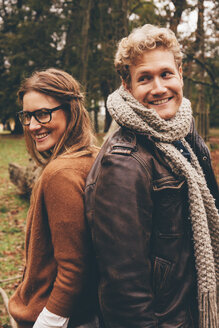 Glückliches junges Paar steht Rücken an Rücken in einem herbstlichen Park - CHAF000205