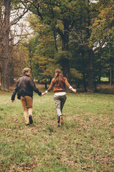 Back view of young couple in love holding hands and running in an autumnal park - CHAF000207