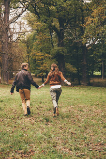 Rückenansicht eines jungen verliebten Paares, das sich an den Händen hält und in einem herbstlichen Park läuft - CHAF000207