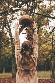 Rückenansicht einer jungen Frau, die sich im Park getrocknete Blätter aus einem Hut auf den Kopf fallen lässt - CHAF000208