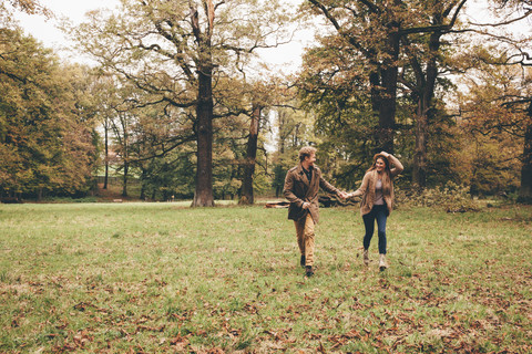 Junges verliebtes Paar, das sich an den Händen hält und in einem herbstlichen Park läuft, lizenzfreies Stockfoto