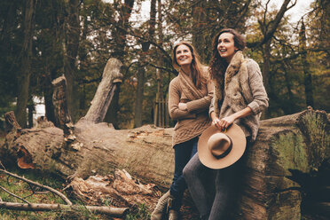 Zwei Freundinnen lehnen an einem Baumstamm in einem herbstlichen Park - CHAF000213