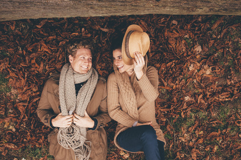 Junges Paar liegt Seite an Seite auf Herbstblättern in einem Park, lizenzfreies Stockfoto