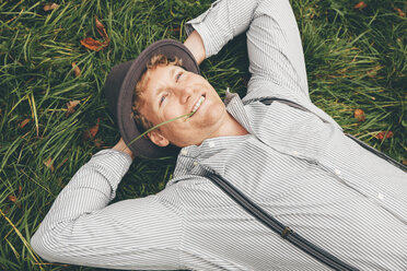 Portrait of smiling young man lying on a meadow with hands behind his head - CHAF000230