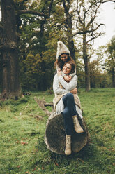 Mother and litte daughter together on a tree trunk in autumnal park - CHAF000252