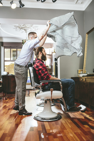 Barbier bindet sich einen Umhang um den Kunden, lizenzfreies Stockfoto