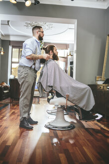 Barbier schneidet Bart eines Kunden und schaut in den Spiegel - MADF000342