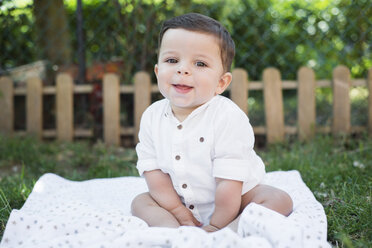 Glücklicher kleiner Junge sitzt auf einer Decke im Garten - RAEF000222