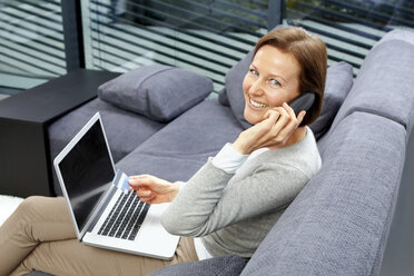 Porträt einer lächelnden Frau, die mit Laptop und Kreditkarte auf einer Couch sitzt und telefoniert - CHAF000270