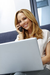 Portrait of smiling young woman with laptop talking on telephone - CHAF000290