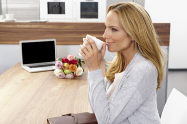 Lächelnde Frau trinkt Kaffee, während sie am Tisch sitzt und wegschaut - CHAF000292