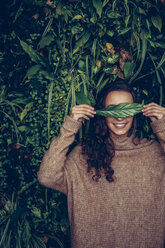 Lächelnde junge Frau, die ihre Augen mit einem Blatt bedeckt - CHAF000330