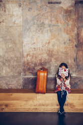 Mädchen sitzt auf einer Bank und liest ein Buch neben einem Koffer - CHAF000335