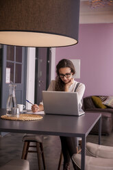 Young woman sitting at table using laptop - CHAF000345