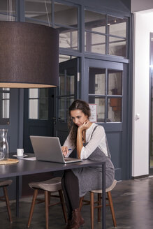 Junge Frau sitzt am Tisch und benutzt einen Laptop - CHAF000346