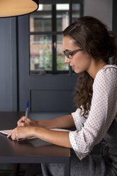 Young woman sitting at table writing on paper - CHAF000348