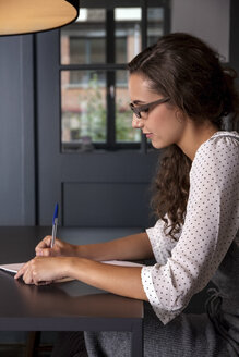 Junge Frau sitzt am Tisch und schreibt auf Papier - CHAF000348