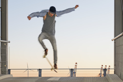 Germany, Hamburg, teenage boy jumping with skateboard on a parkdeck ramp stock photo