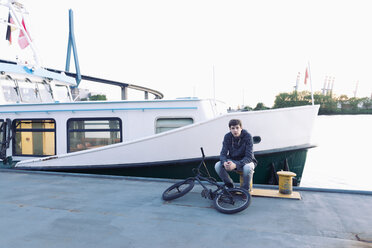 Germany, Hamburg, teenage boy with bmx bike sitting on a jetty - MEMF000814