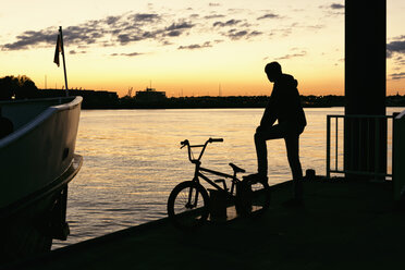 Deutschland, Hamburg, Silhouette eines jungen Mannes mit Fahrrad auf einem Steg im Abendlicht - MEMF000816