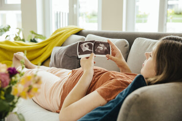 Pregnant woman looking at ultrasound scan while relaxing on the couch - MFF001809
