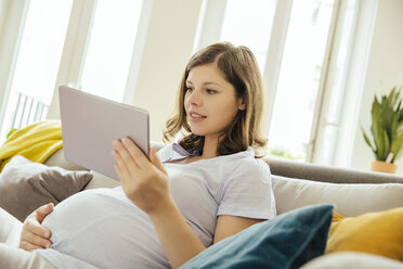 Schwangere Frau mit digitalem Tablet entspannt sich auf der Couch zu Hause - MFF001784