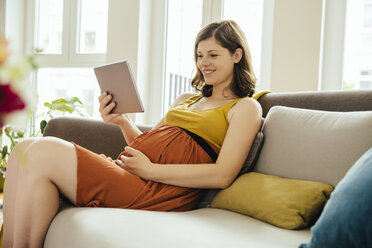 Schwangere Frau mit digitalem Tablet entspannt sich auf der Couch zu Hause - MFF001787