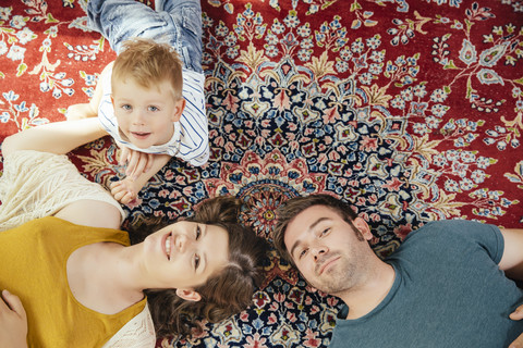 Gruppenbild von Eltern und kleinem Sohn, die zu Hause auf einem Perserteppich liegen, lizenzfreies Stockfoto