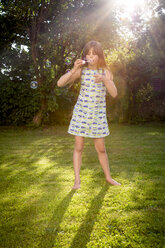Girl blowing soap bubbles in a garden - LVF003613