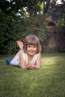Lächelndes kleines Mädchen auf der Wiese im Garten liegend - LVF003616