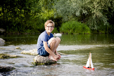 Junge spielt mit hölzernem Spielzeugboot an einem Fluss - LVF003621