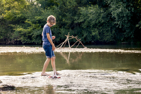 Junge spielt mit hölzernem Spielzeugboot an einem Fluss - LVF003622