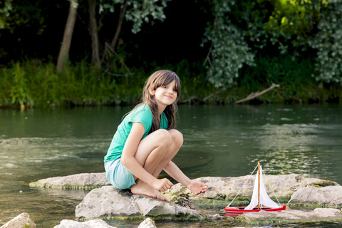 Girl playing with wooden toy boat at a river stock photo