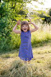Portrait of little girl standing in hay field making faces - LVF003629